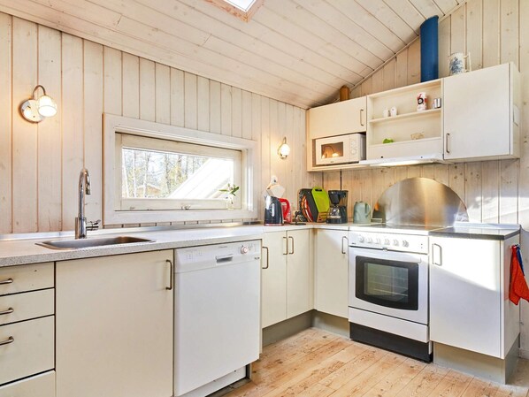 Una cocina con paredes de madera, una ventana, un lavabo, un lavavajillas, un microondas, una estufa y un estante con utensilios de cocina.