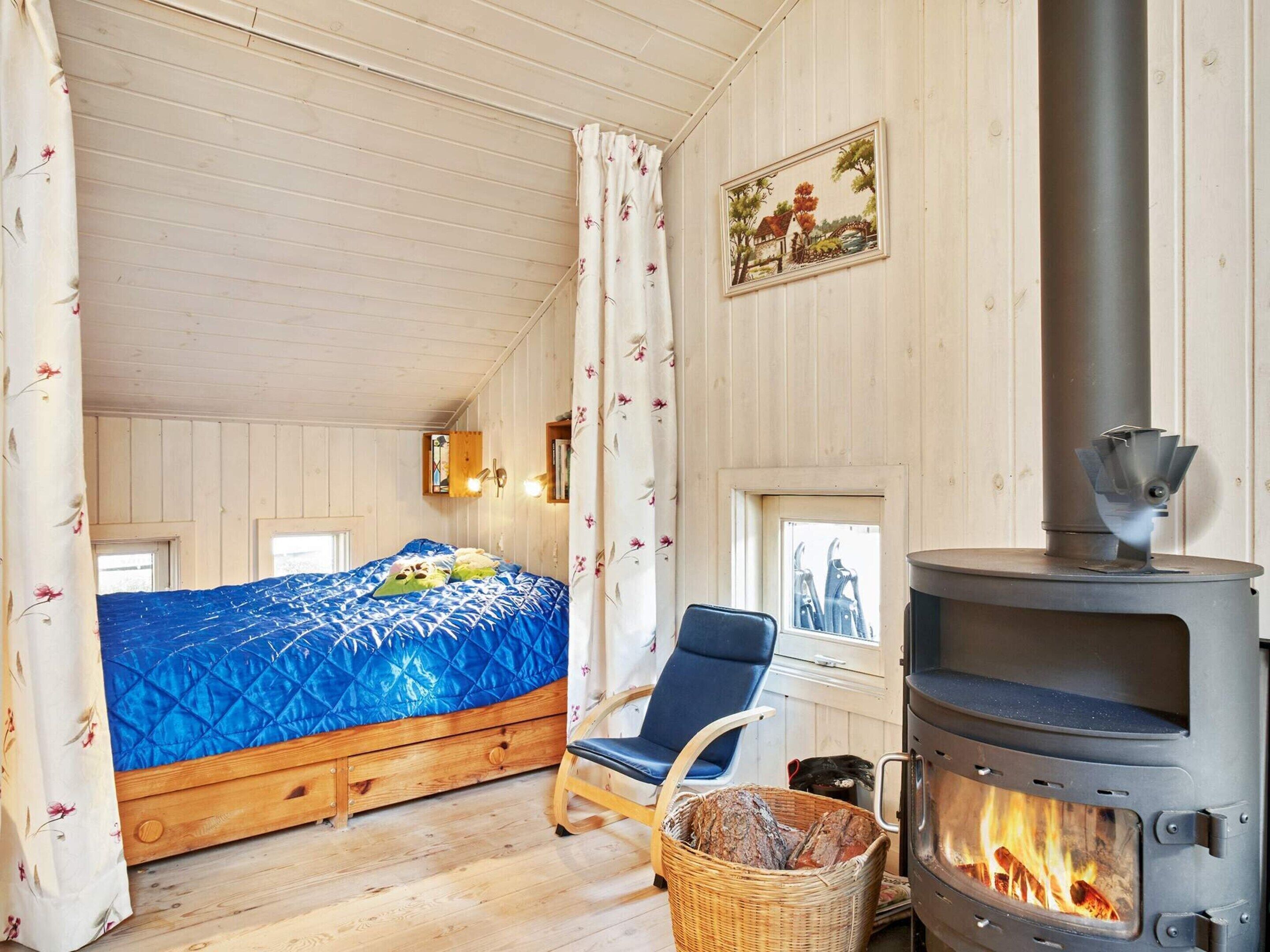 A cozy room with a bed, a chair, a fireplace, and a window.