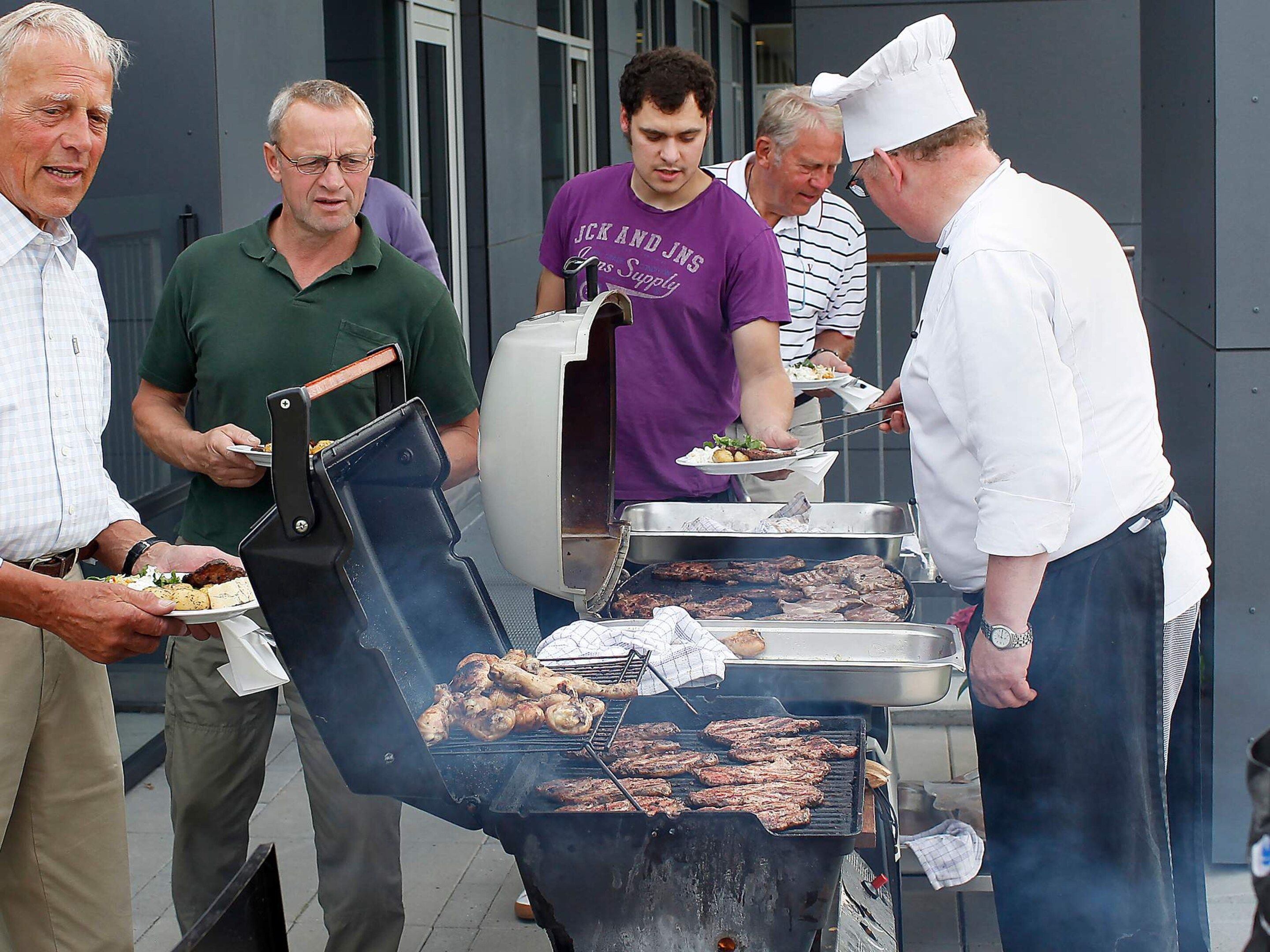 Un groupe de personnes rassemblées autour d’un barbecue où de la nourriture est en train de cuire.