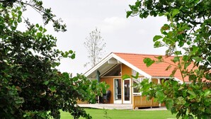 Una casa de fusta amb teulada vermella, un porxo cobert i un jardí en verd.