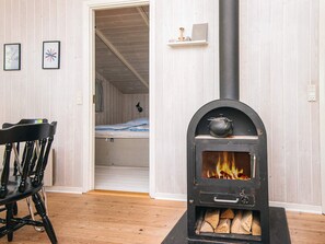 Una habitación con un estufa de leña negra, una silla de madera y una cama con manta a rayas.
