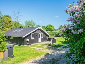 A single-story building with a sloped roof, a front door, and a small patio area with a table and chairs.