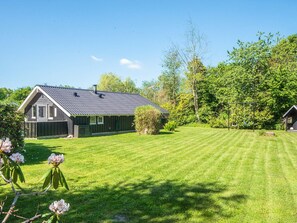 Een huis met schuin dak, omheinde tuin en een schommel.
