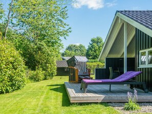 A wooden deck with a lounge chair and a striped umbrella, surrounded by greenery and a building with a sloped roof. - 4 Star Holiday Home in Borkop (Borkop)