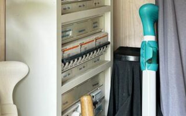 A storage area with shelves containing various items, a black trash bin, and a teal cleaning tool.