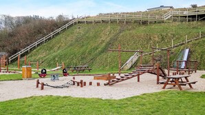 A playground with wooden structures, a slide, and picnic tables on a grassy hill. - 5 Person Holiday Home in Lemvig-by Traum (Lemvig)