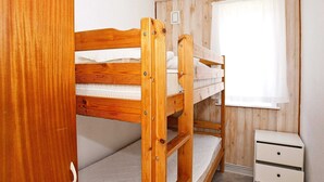 Habitació amb lliteres, un panell de fusta al capçal, una petita taula de nit amb calaixos i una finestra amb cortines.