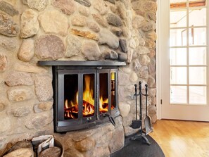 A stone fireplace with a modern wood-burning stove, a fire burning inside, and a door leading to an outdoor area. - 5 Star Holiday Home in Logstrup (Logstrup)