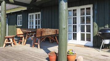 A wooden deck with a table and chairs, a barbecue grill, and potted plants.