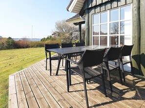An outdoor deck with a table and chairs, a view of the sea, and a building with large windows. - 5 Star Holiday Home in Logstrup (Logstrup)