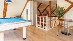 A pool table with a blue felt surface, a dining area with a wooden table and chairs, and a staircase with wooden beams. - 5 Star Holiday Home in Logstrup (Logstrup)