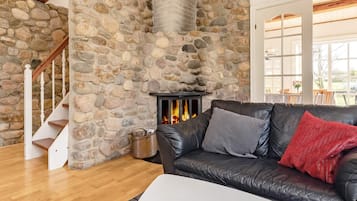 Una pared de piedra, una chimenea, un sofá de cuero y una escalera de madera.