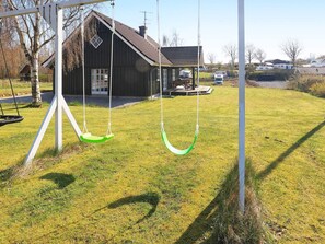 A swing set with two swings, a wooden house with a porch, and a grassy yard. - 5 Star Holiday Home in Logstrup (Logstrup)