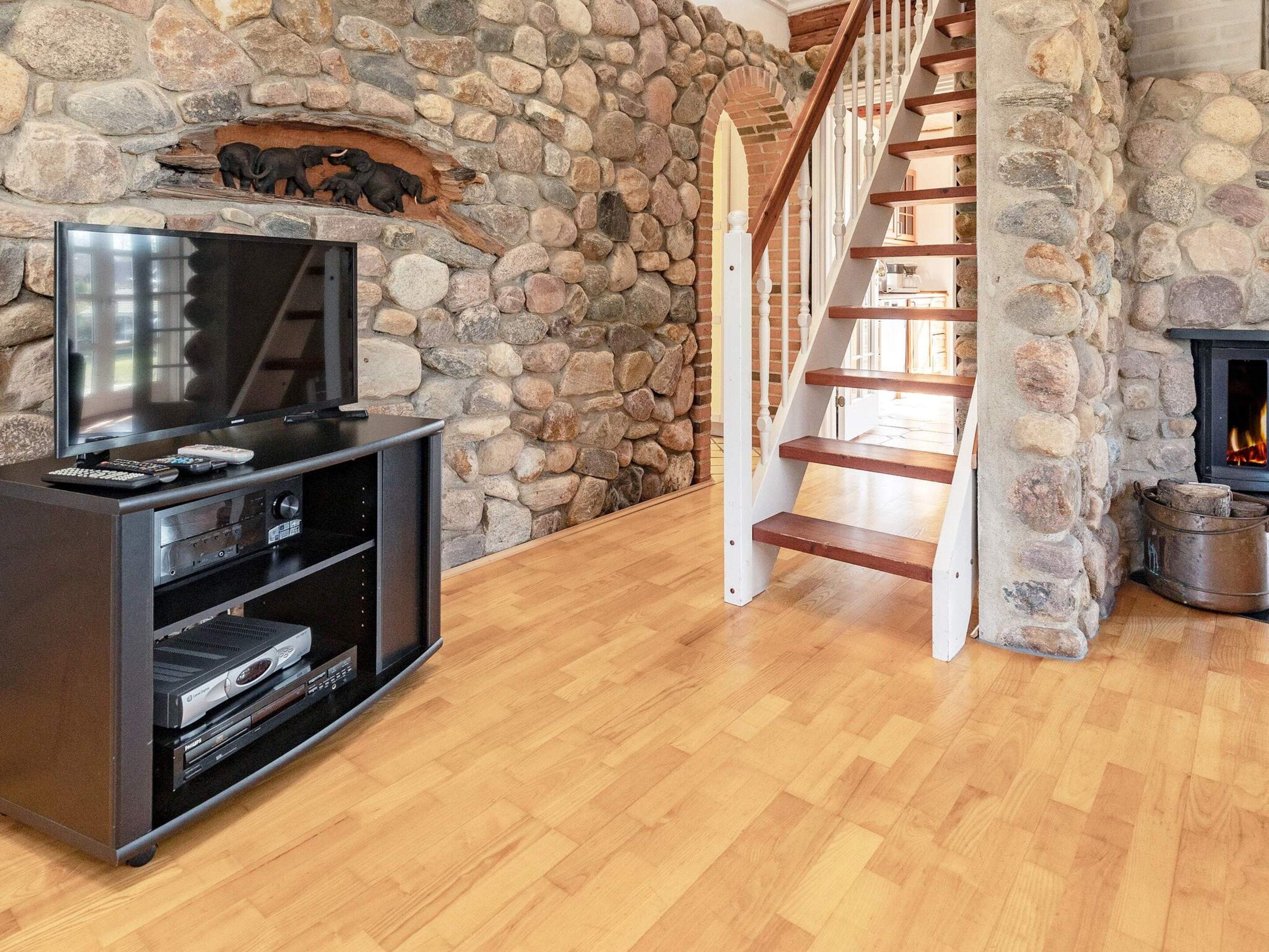 A stone wall, a wooden staircase, and a television stand with a fireplace.