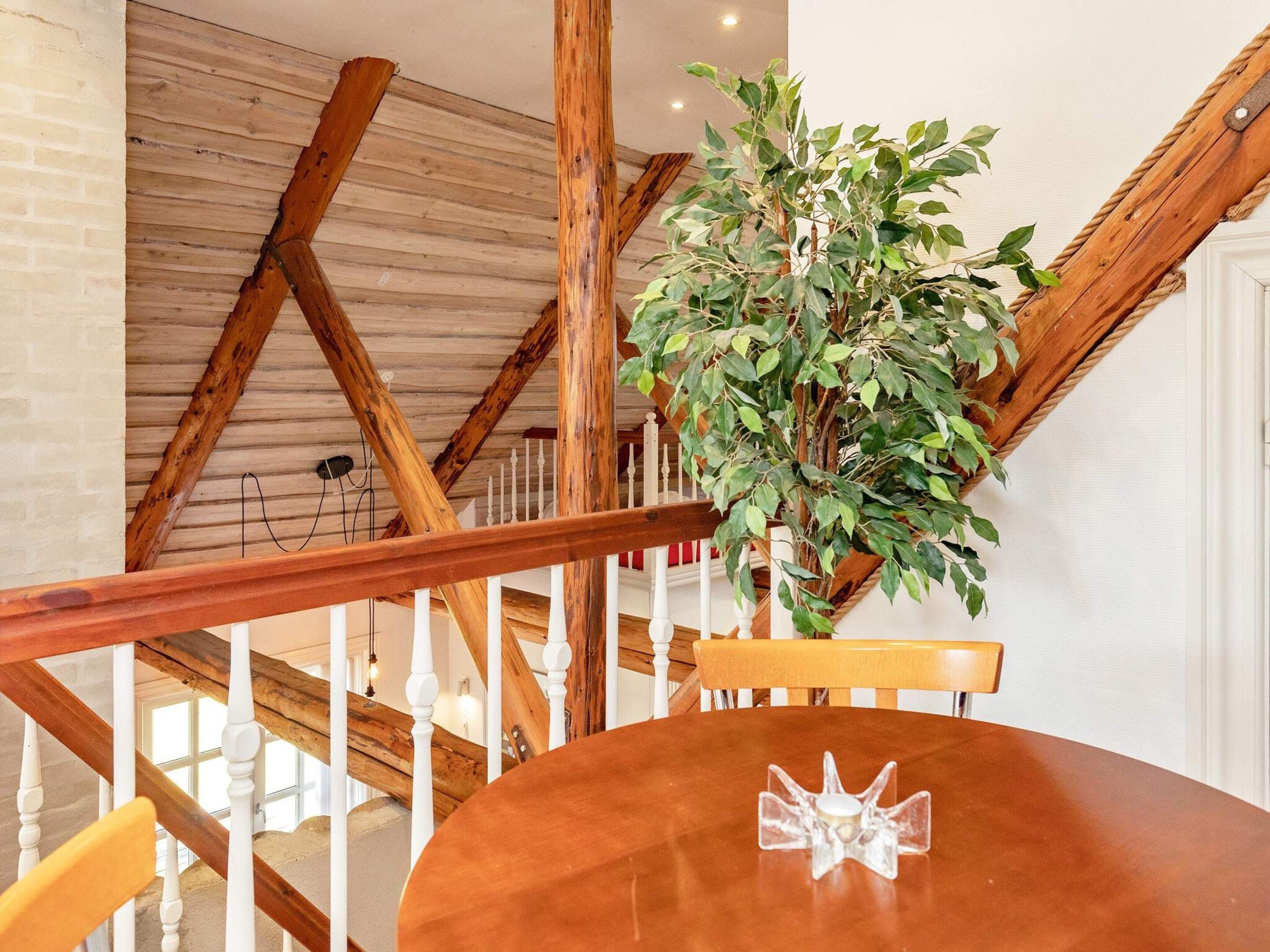 A wooden staircase with white balusters, a round wooden table with a clear glass centerpiece, and a potted plant.