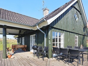 A wooden deck with outdoor furniture, a barbecue grill, and a large window.