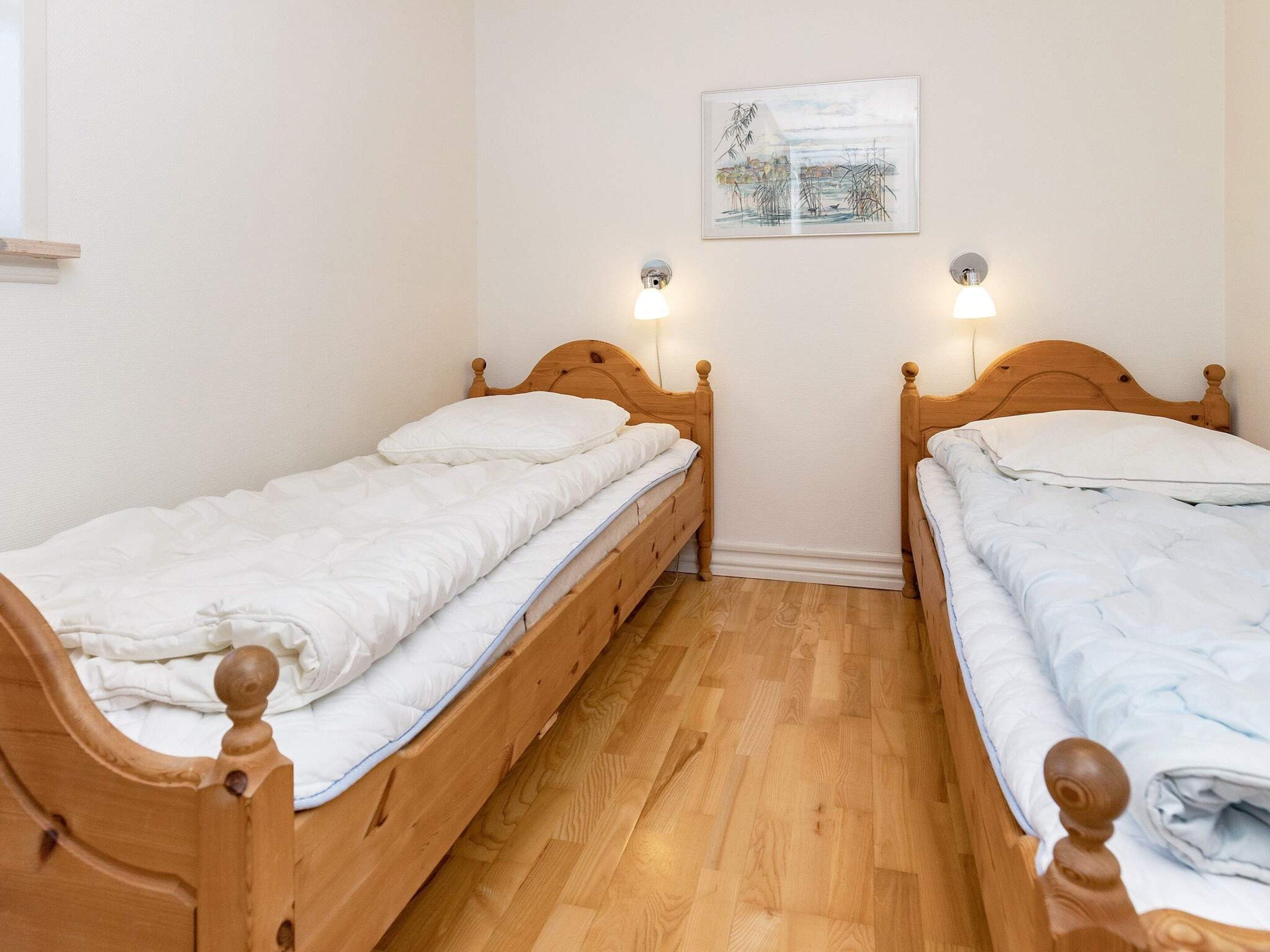 A room with two wooden beds, a white wall, and a framed picture.
