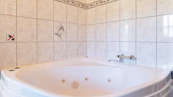 Un baño con una bañera grande, paredes con azulejos y un detalle decorativo.