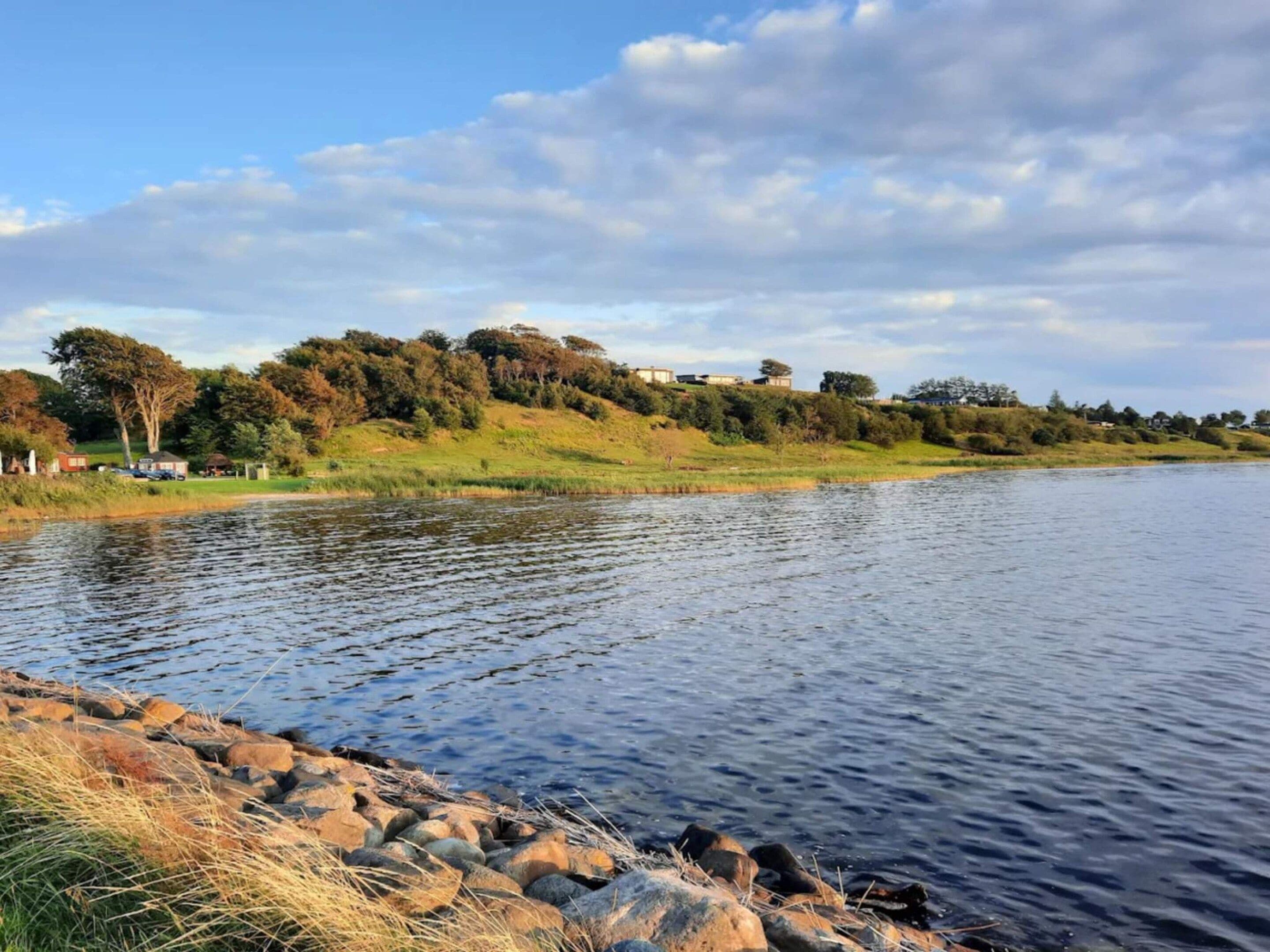 A calm lake with a rocky shoreline and a grassy bank.