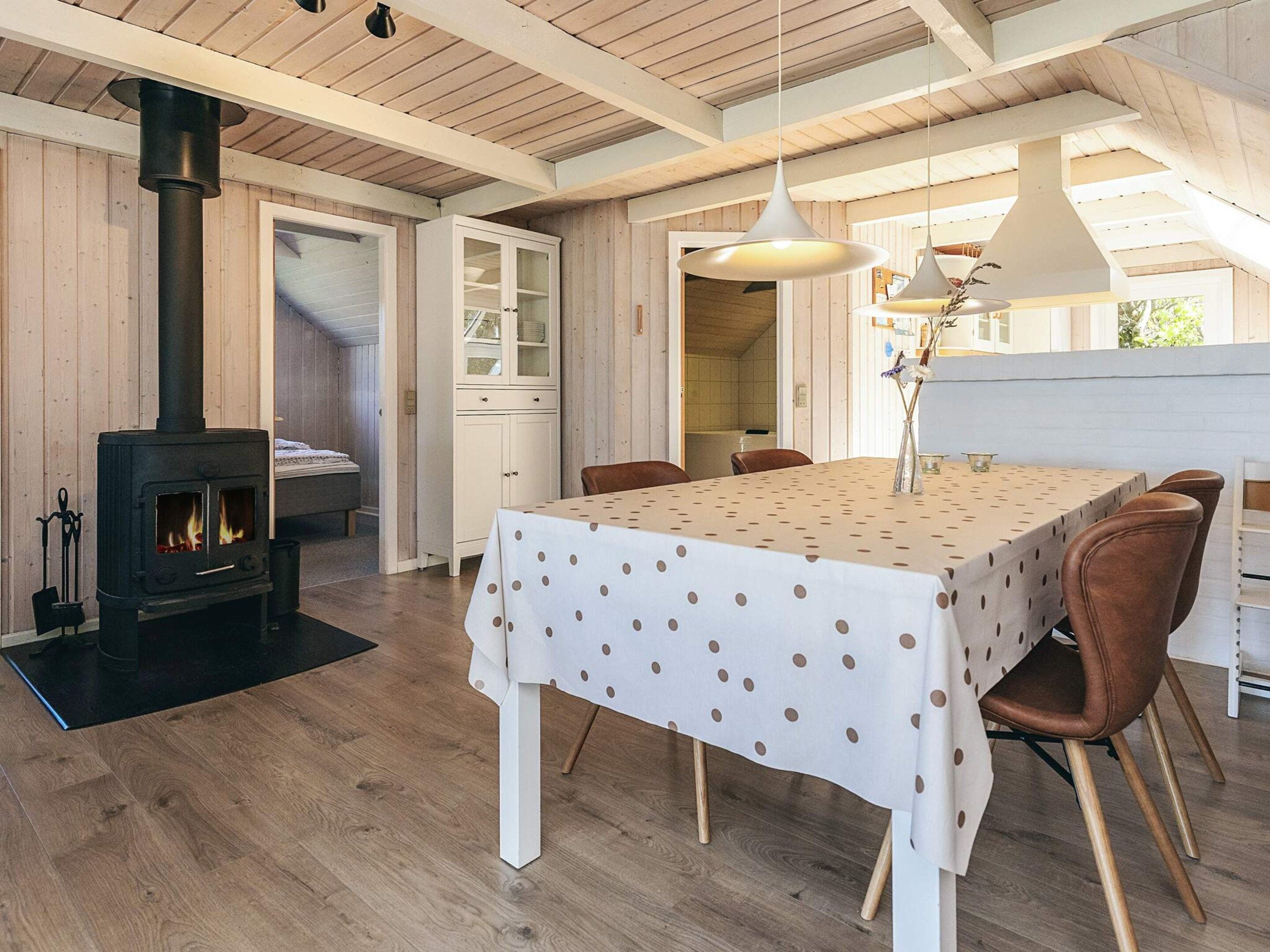 Une pièce chaleureuse avec une table centrale, des chaises, un buffet blanc et un poêle à bois.
