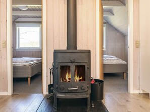 A room with a wood-burning stove, two beds, and a window.