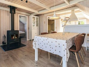 A cozy room with a wood-burning stove, a dining table with chairs, and a hanging light fixture.