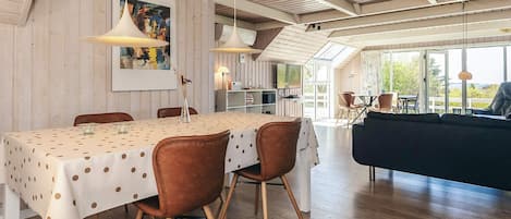 A dining area with a table set for four, wooden chairs, pendant lighting, and a view of the outdoors.