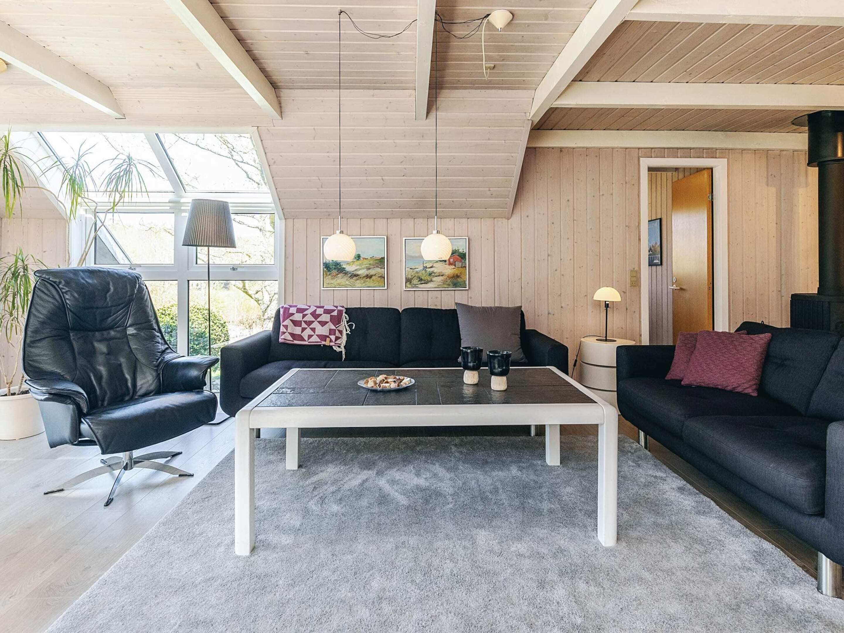 A modern living room with a sofa, armchair, and coffee table, wooden walls, and a large window.