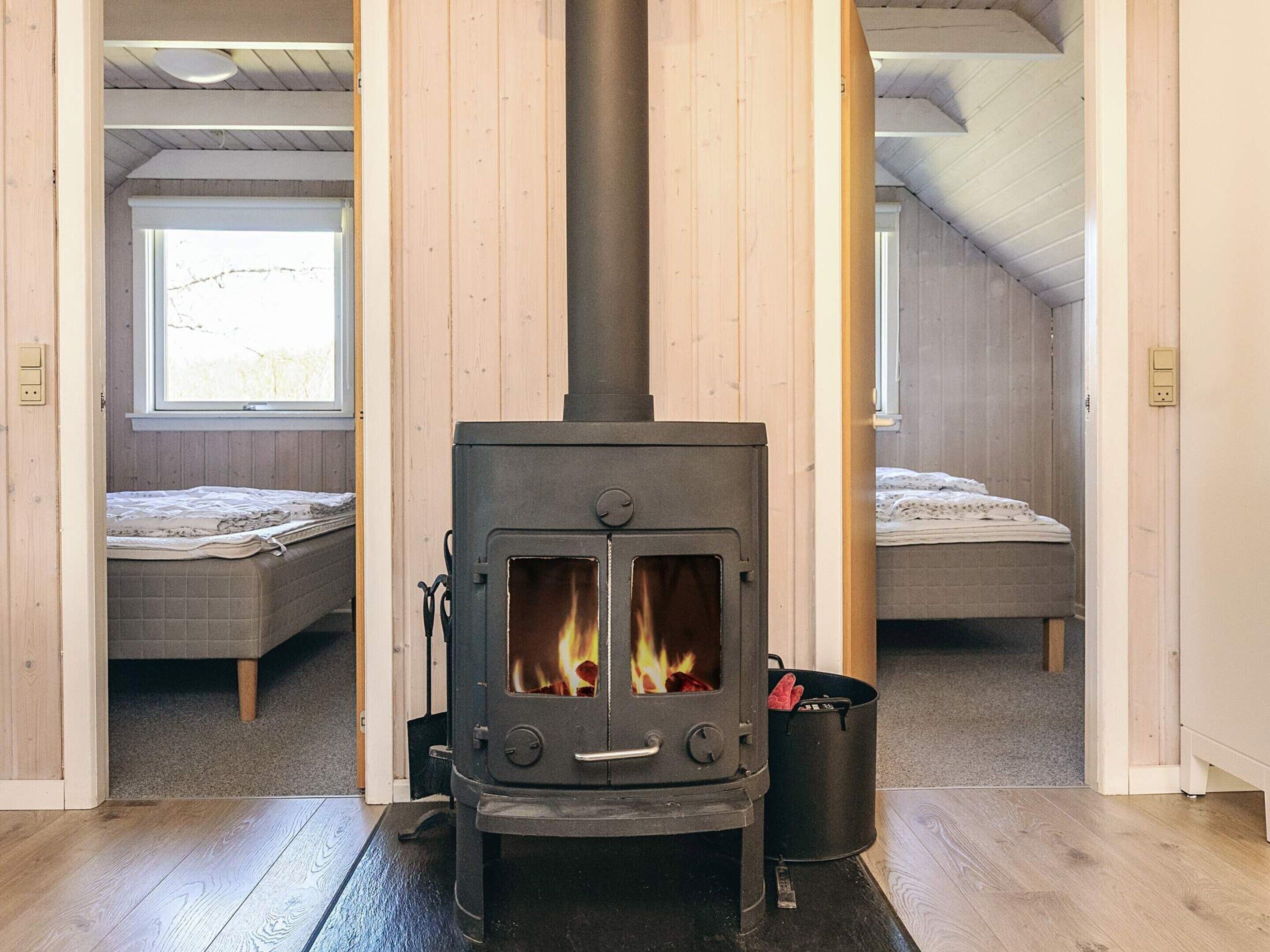 A room with a wood-burning stove, two beds, and a window.