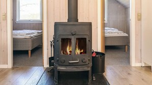 A room with a wood-burning stove, two beds, and a window.