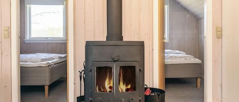 A room with a wood-burning stove, two beds, and a window.