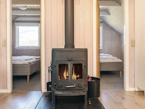 A room with a wood-burning stove, two beds, and a window.