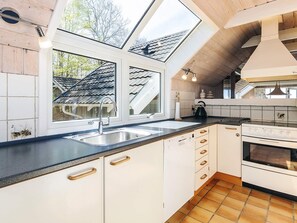A modern kitchen with a skylight, white cabinets, a black countertop, and a stove.
