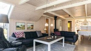A modern living room with a sofa, armchair, and coffee table, wooden flooring, and a high ceiling with exposed beams.