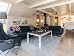 A modern living room with a sofa, armchair, and coffee table, wooden flooring, and a high ceiling with exposed beams.