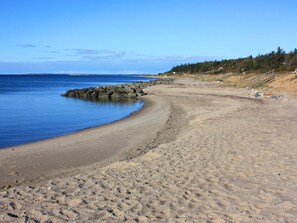A sandy beach with a calm sea, rocky outcrops, and a forested hillside.