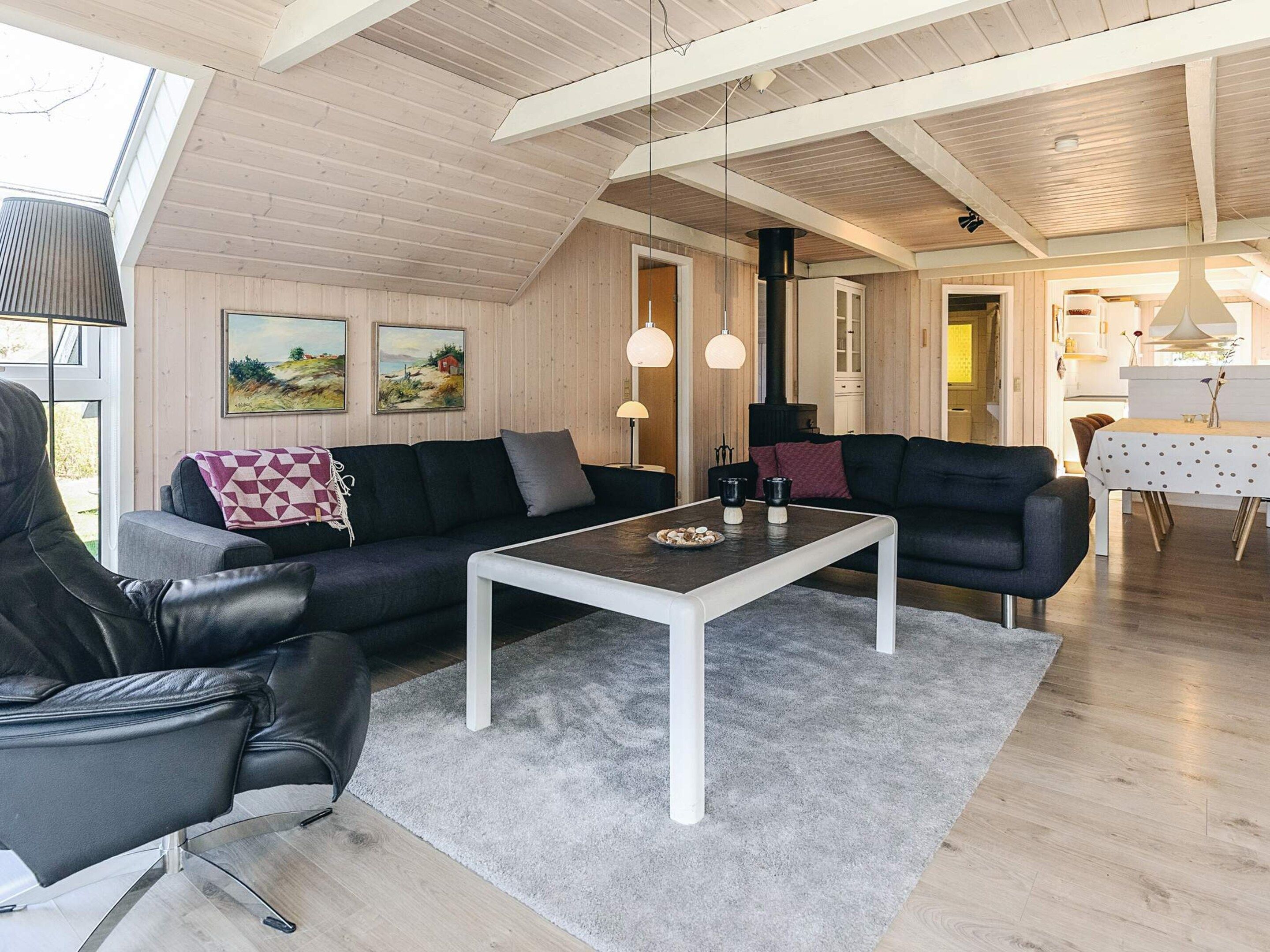 A modern living room with a sofa, armchair, and coffee table, wooden flooring, and a high ceiling with exposed beams.