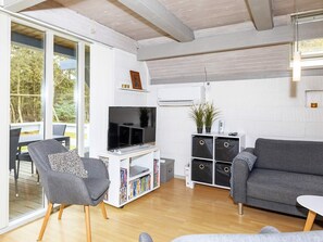 A modern living room with a grey sofa, a grey armchair, a flat-screen TV on a white stand, and a bookshelf filled with books. - Swanky Seaside Holiday Home in Fur near Sea (Fur)