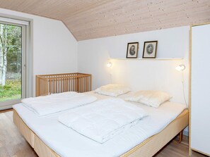 A bedroom with a large bed, two bedside lamps, a crib, and a window with a view of trees. - Swanky Seaside Holiday Home in Fur near Sea (Fur)