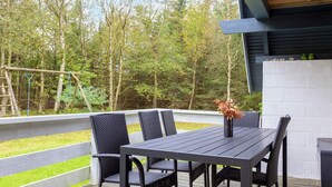 An outdoor deck with a table and chairs, surrounded by a wooden deck and a view of trees. - Swanky Seaside Holiday Home in Fur near Sea (Fur)