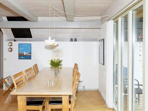 A dining area with a wooden table, chairs, a vase with flowers, pendant lights, and a view through a glass door. - Swanky Seaside Holiday Home in Fur near Sea (Fur)