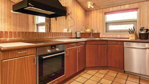 A kitchen with wooden cabinets, a stainless steel dishwasher, a built-in oven, and a black range hood. - 5 Star Holiday Home in Hadsund (Hadsund)
