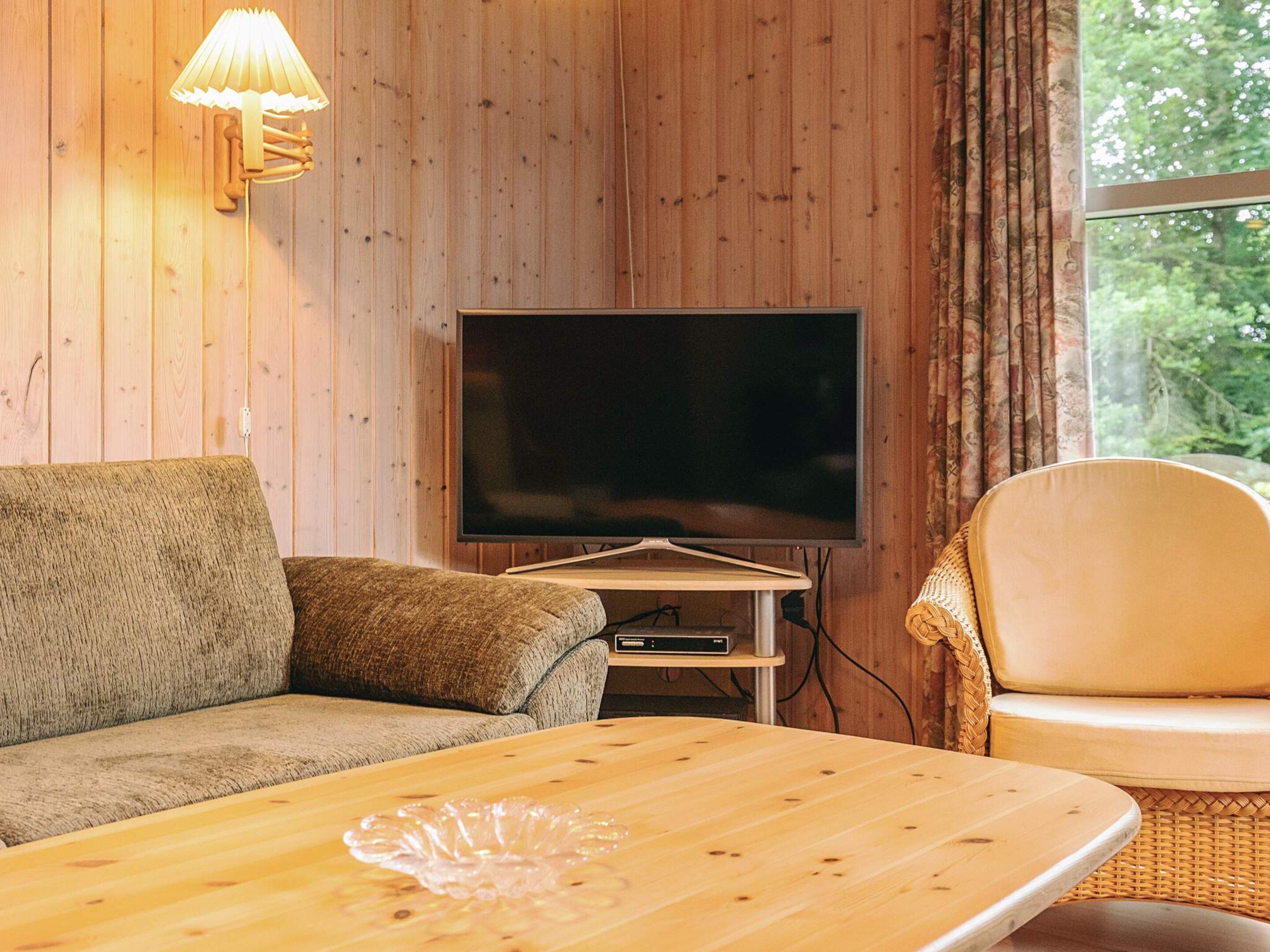 Un soggiorno con parete in legno, televisione a schermo piatto, divano, tavolino da caffè e una poltrona in vimini.