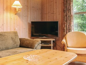 A living room with a wooden wall, a flat-screen TV, a sofa, a coffee table, and a wicker chair.