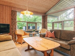 Een gezellige woonkamer met een houten plafond, een televisie, rieten meubels, een bank en een salontafel.