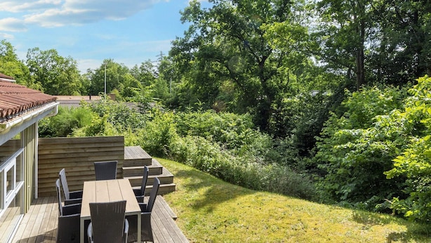 A wooden deck with outdoor furniture, surrounded by lush greenery and trees. - 5 Star Holiday Home in Hadsund (Hadsund)