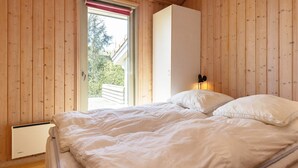 A bedroom with a wooden ceiling, a bed with white bedding, a radiator, and a window with a red blind. - 5 Star Holiday Home in Hadsund (Hadsund)