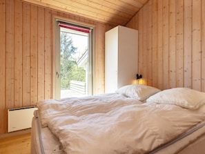 Une chambre avec un plafond en bois, un lit avec une literie blanche, un radiateur et une fenêtre avec un store rouge.