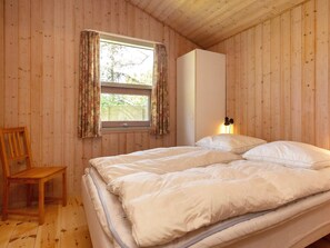 Una habitación con paredes de madera, una cama con ropa de cama blanca, una silla y una ventana con cortinas.