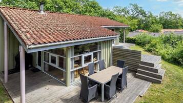 A house with a tiled roof, a deck with outdoor furniture, and a view of the surrounding greenery.